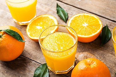 Изцеден портокалов сок в чаша и пресни портокали