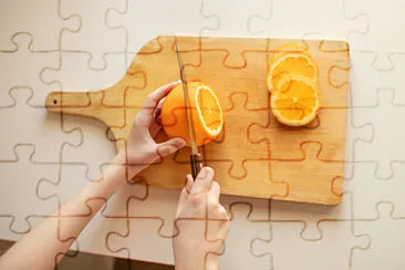 Hand slicing orange on wooden board jigsaw puzzle